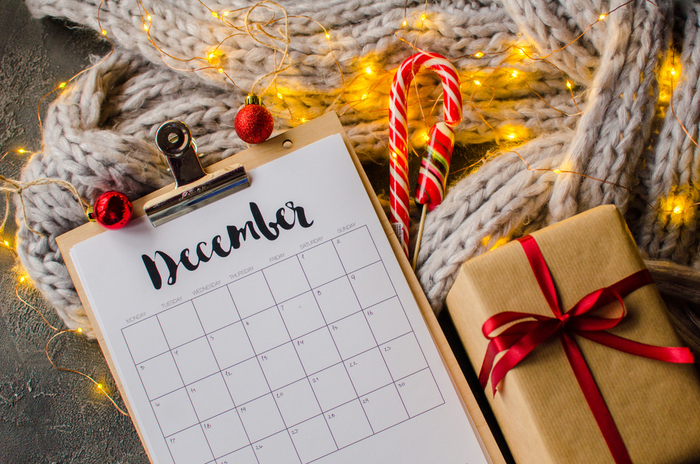 A calendar for December next to a present, candy cane and Christmas lights.