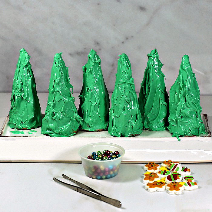 Making Christmas trees out of waffle cones. Waffle cones covered in green frosting with tweezers, and candy decorations.