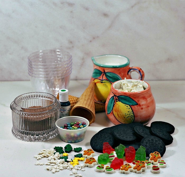 ingredients for dirt pudding for Christmas Plastic cups, frosting, milk, Oreos and various Christmas sprinkles and decorations.