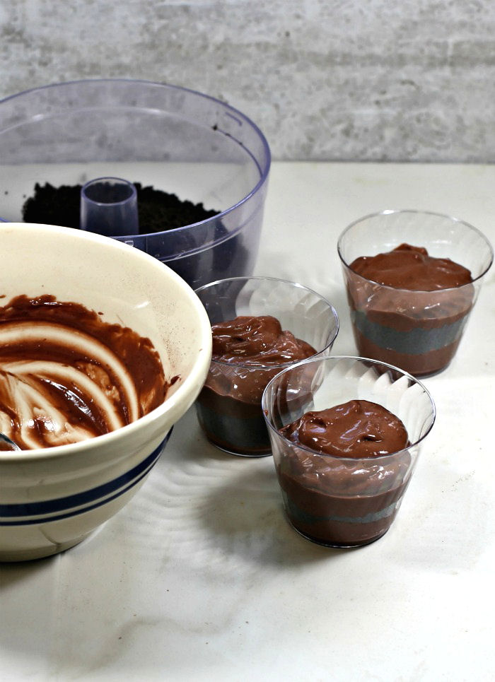 Layering dirt pudding Chocolate pudding and dirt crumbs layered in plastic cups for dirt puding.