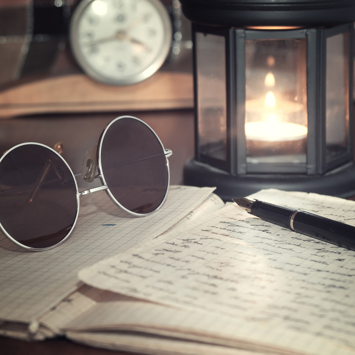 Handwritten letters, a candle, clock and sunglasses arranged on a table to celebrate National Letter Writing Day.