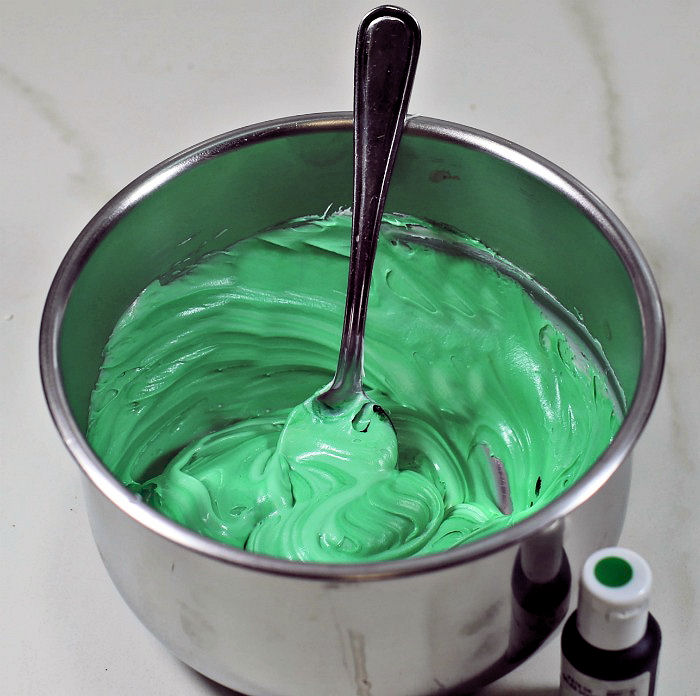 tinting frosting green. Frosting in a bowl tinted green with a spoon and gel paste coloring bottle.