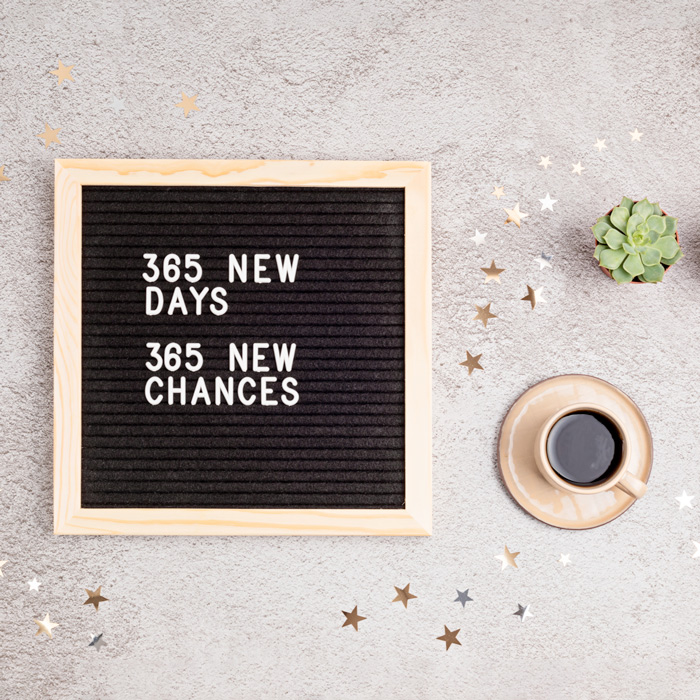 A message board reading "365 new days, 365 new chances" on a white counter next to a cup of coffee and a succulent to celebrate Stick to Your New Year's Resolutions Day.