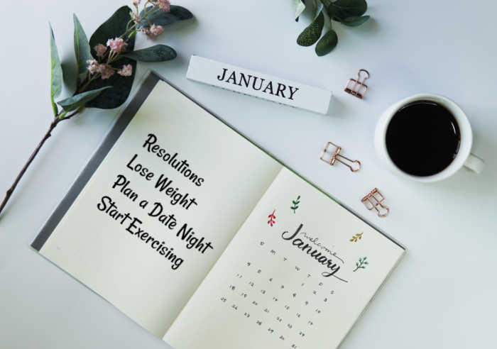 Let's form some New Years Resolutions. Calendar, flowers and coffee cup with a January journal with new years resolutions.
