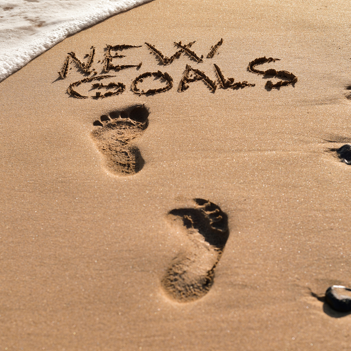Footprints on the beach leading to the text "new goals" to celebrate Stick to Your New Years Resolution Day.