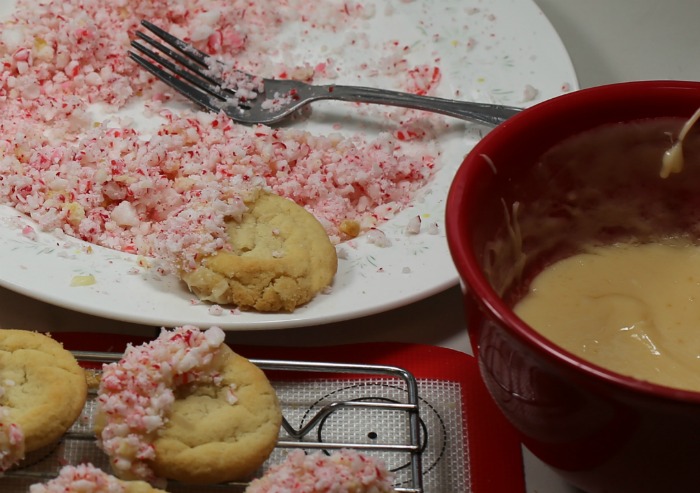 Adding peppermint crumbs to sugar cookies. Adding peppermint crumbs to melted chocolate on sugar cookies.