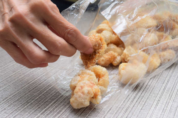 eating pork rinds. Hand taking pork rind out of a plastic bag. Celebrate National Pork Rind Appreciation Day.