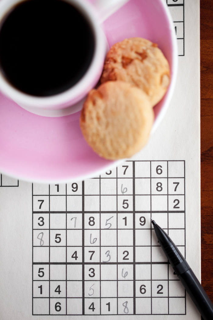 Coffee, biscotti and a Sudoku puzzle. A cup of coffee and biscotti sitting on a pink plate near a Sudoku puzzle to celebrate National Puzzle Day.