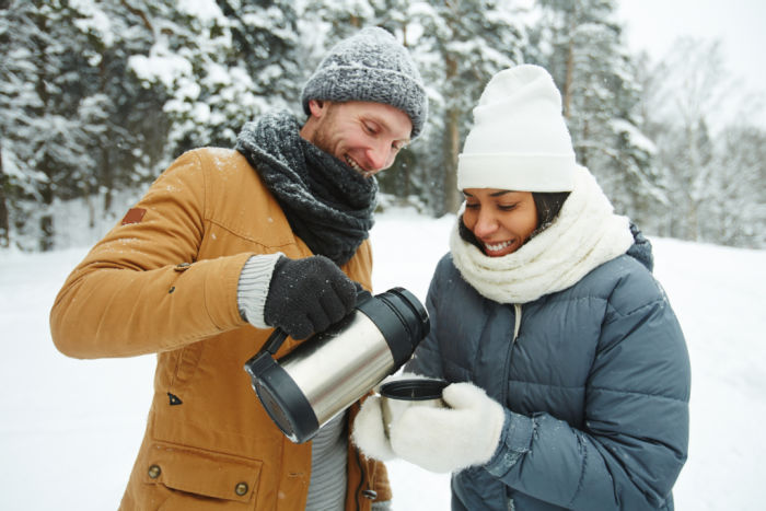 Time for coffee in the snow. Man and woman on cold weather gear sharing a thermos.