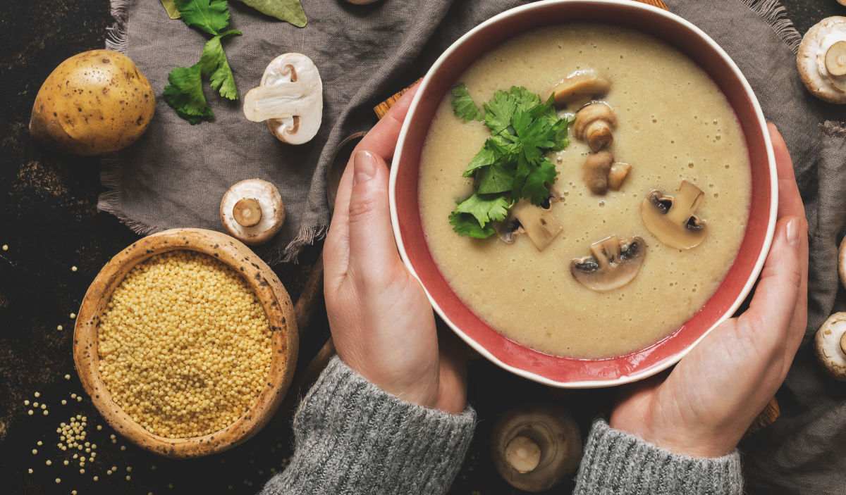 Food for January! Hands holding a bowl of soup with potato, couscous, and mushrooms.