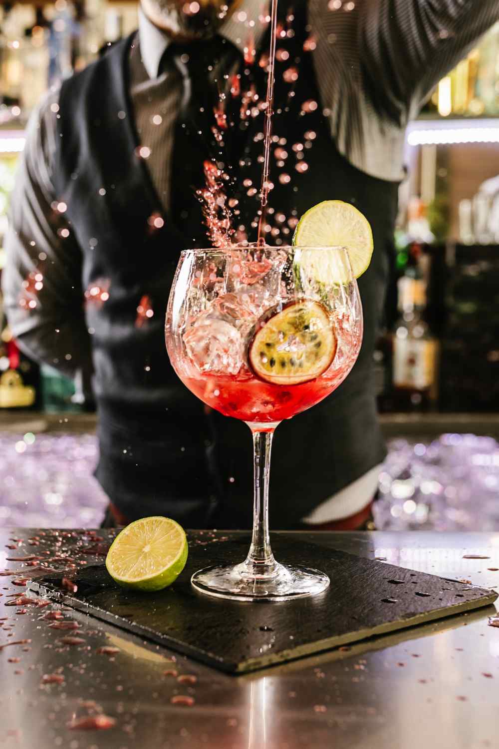 A man in a suit making a pink cocktail behind a bar to celebrate bartending history.
