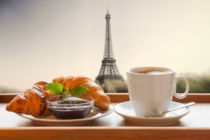A cafe au lait and croissant with the Eiffel Tower in the background to celebrate the cafe au lait meaning.