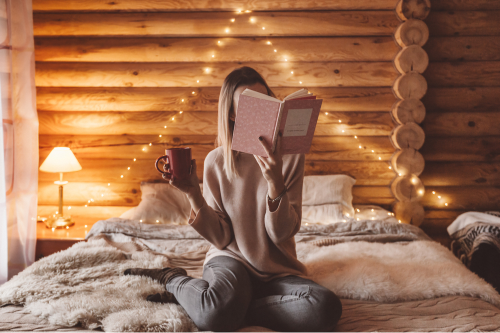 A woman reading a book on a bed to celebrate Clean Out Your Bookcase Day.