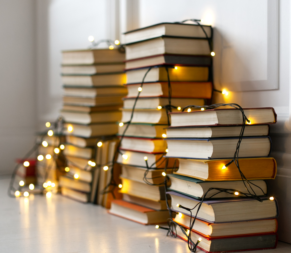 Four piles of books with twinkle lights draped over them.