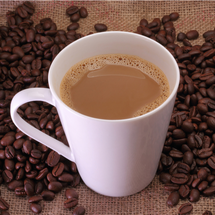 A cafe au lait in a white cup with coffee beans around it.