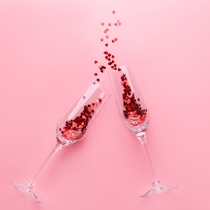 Two champagne flutes toasting with pink glitter to celebrate what is Galentine's Day.