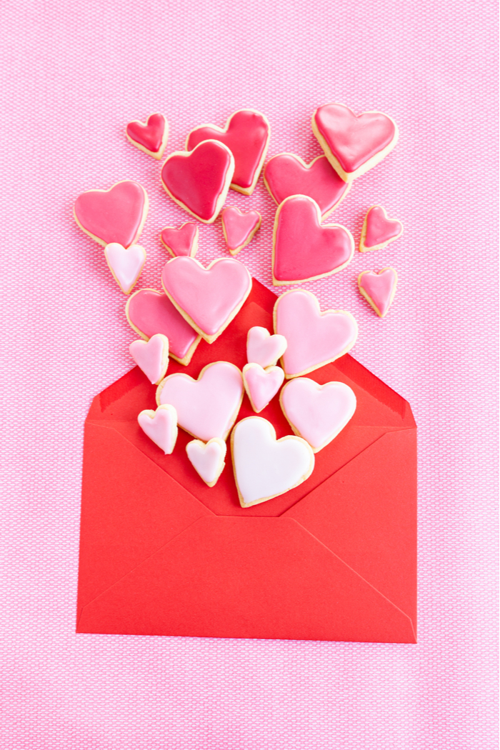 A red envelope with heart shaped cookies coming out of it to celebrate when is Galentine's Day.
