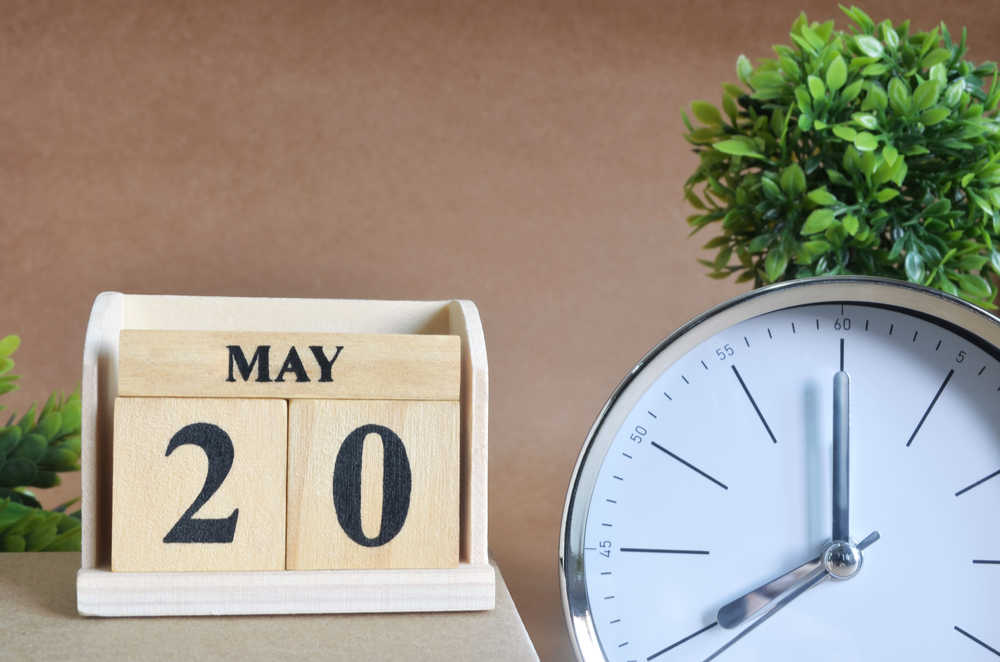 Close up shot of blocks that say May 20 next to a clock on a desk.