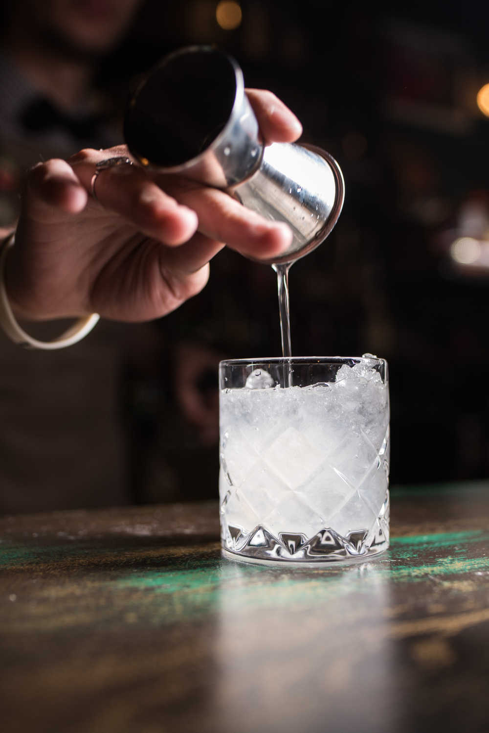 Bartender pouring vodka over ice. A bartender pouring vodka into a short glass over ice using a jigger for National Vodka Day.