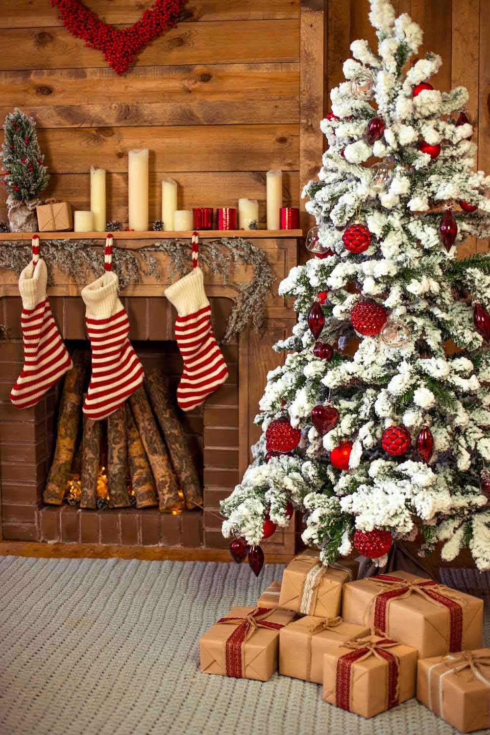 A cozy living room with a flocked tree, a fire filled with wood, three striped stockings and candles on the mantle.
