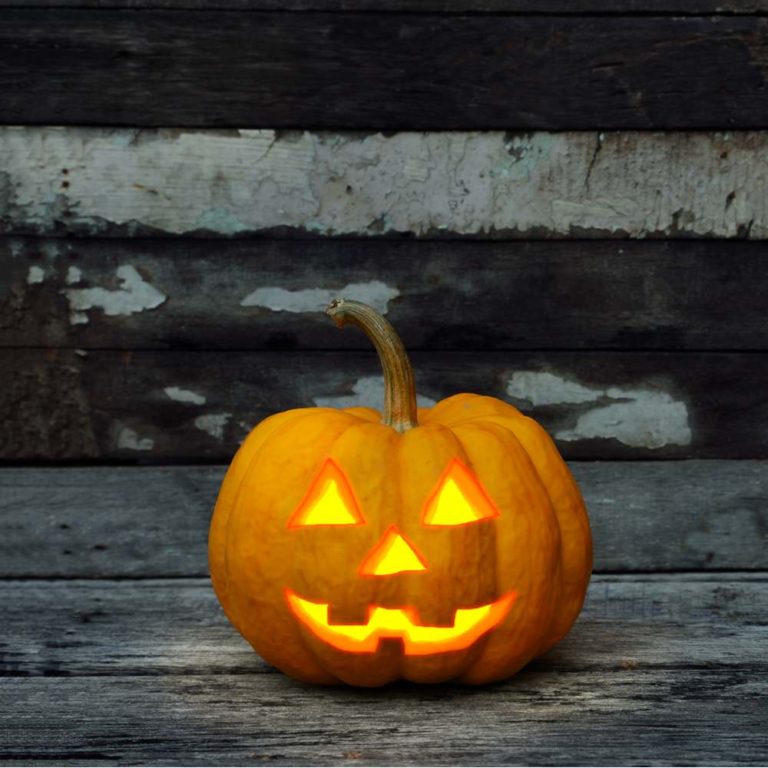 A small lit up jack o lantern against a wall that has light grey and dark grey wooden boards.