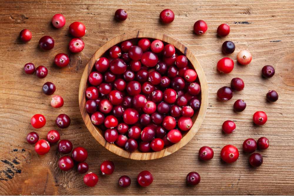 Bowl of cranberries. A bowl of fresh cranberries on a wooden table with some cranberries scattered around the bowl.