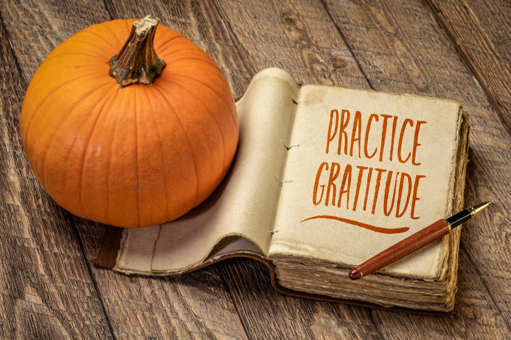 A pumpkin and journal with the words "practice gratitude" on it, on a wooden tabletop.