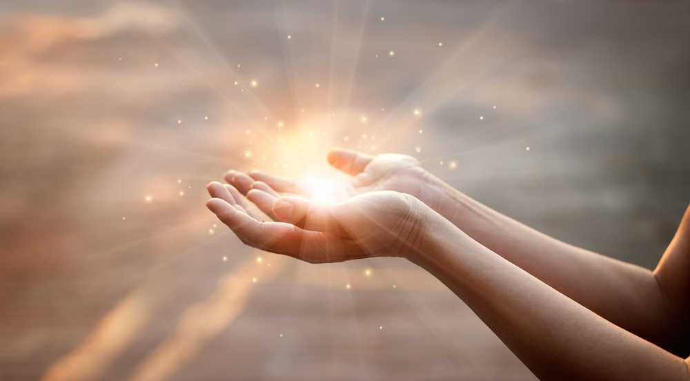 Two hands turned up to the heavens with a bright light of prayer in them.