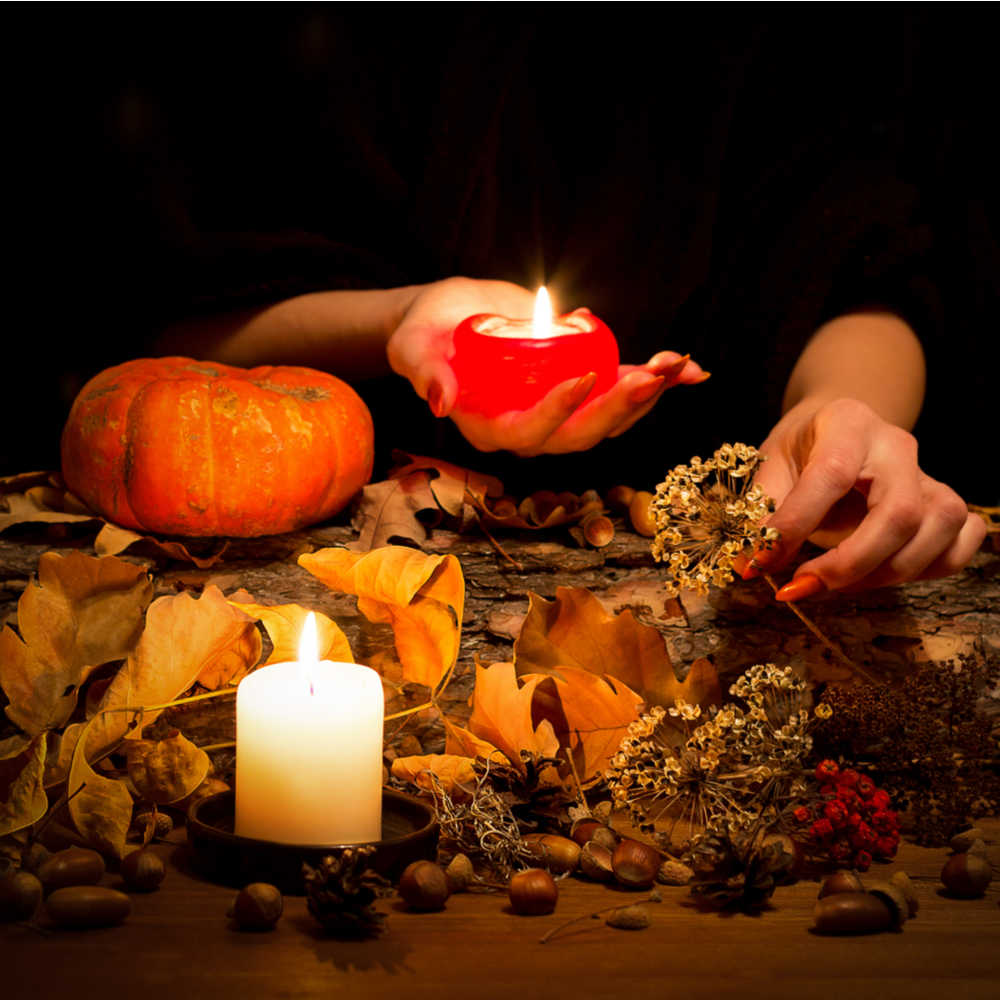 Woman setting up altar for Samhain. A woman holding a pumpkin candle and setting up an alter of fall items for a Samhain tradition.
