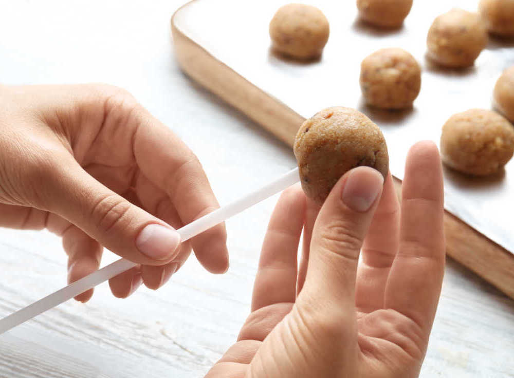 Hands inserting stick into a cake ball.