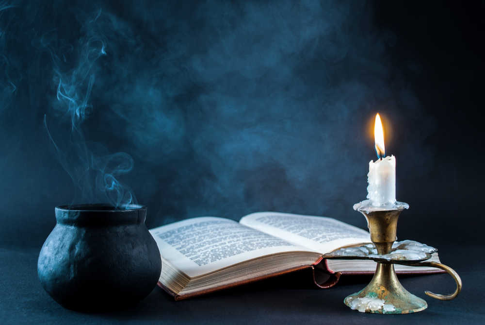 A cauldron, book about the origin of Halloween, and a lit candle against a black background laid out as the start of a Halloween ritual.