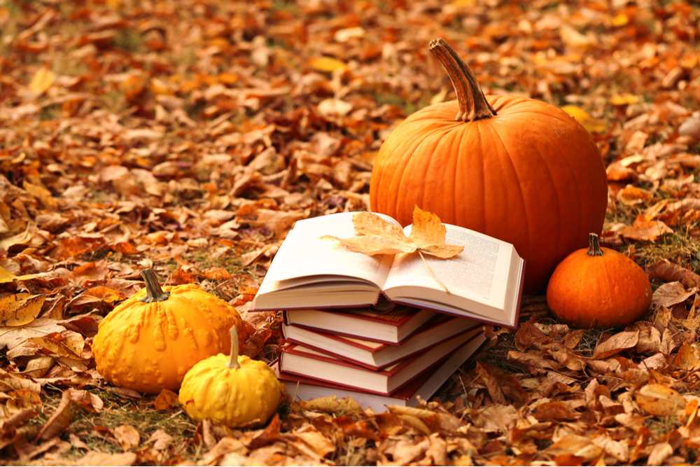Pumpkins and books in field. Four pumpkins in a field of leaves next to a stack of books.