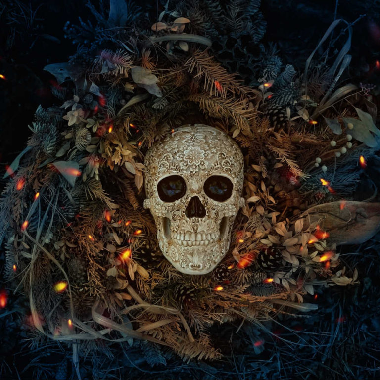 A spooky human skull in a pile of fall leaves and embers to celebrate the history of Samhain.