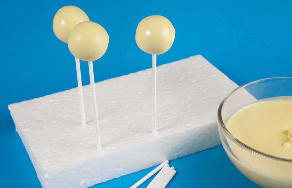 Cake balls coated in white chocolate in Styrofoam setting.
