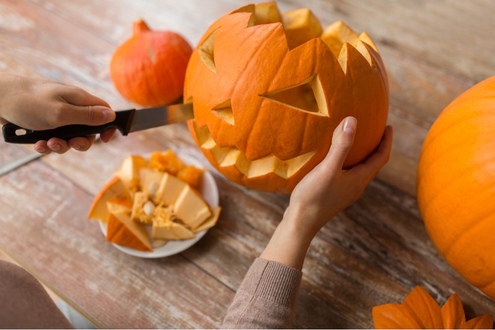 Carving a pumpkin. A woman's hands carving a jack o lantern on a table with a knife.