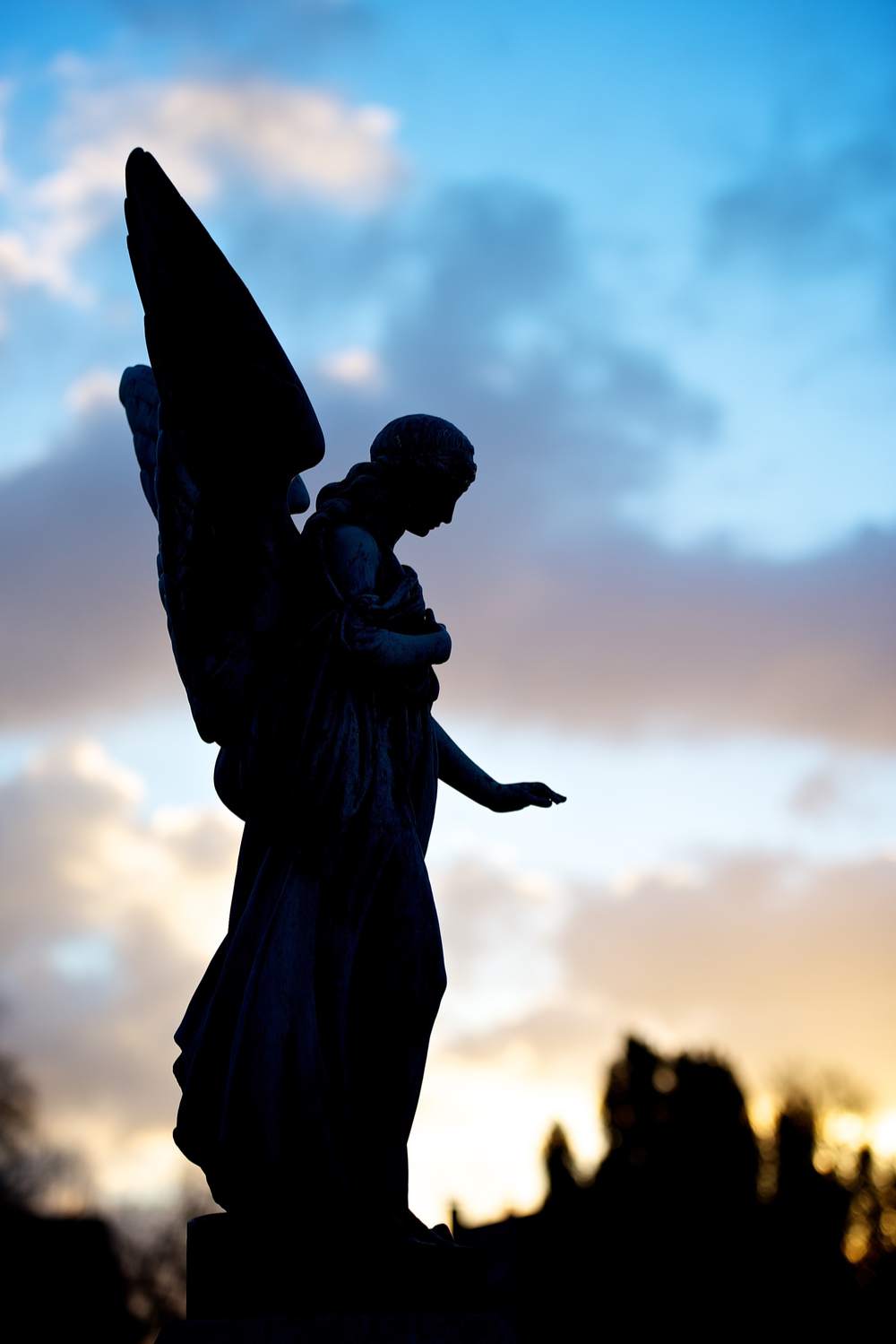 The statue of an angel at sunset with the sky lit up, and the statue in shadow.