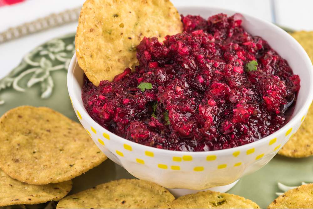 Cranberry relish with chips. A bowl of fresh cranberry relish with chips around it on a green plate to illustrate what is cranberry relish.
