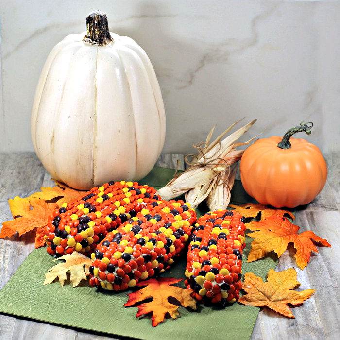 Indian corn dessert. A dessert corn Thanksgiving recipe that looks like ears of corn on a green place mat surrounded by fake orange leaves and a fake white pumpkin and fake orange pumpkin.