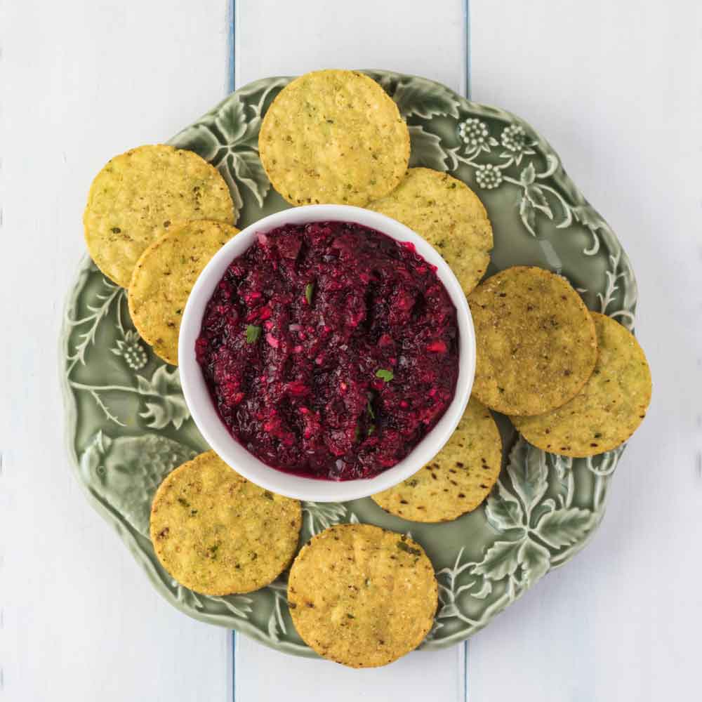 Cranberry relish and chips. A cranberry recipes for Thanksgiving consisting of cranberry relish in a ramekin and corn chips around it on a green plate.