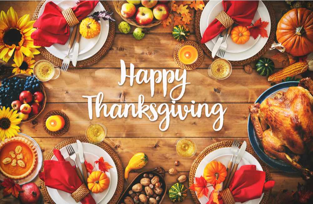 Happy Thanksgiving text and beautiful Thanksgiving table. A table with the words Happy Thanksgiving in the center and four plates in the corners with silverware rolled in napkins, pumpkins, nuts and other symbols of Thanksgiving scattered around the table artistically.