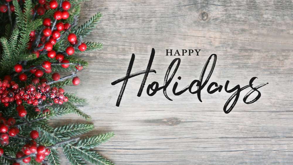 Happy holidays text and greenery. Fir boughs and berries on a grey wooden backdrop with text over it that reads "Happy Holidays".