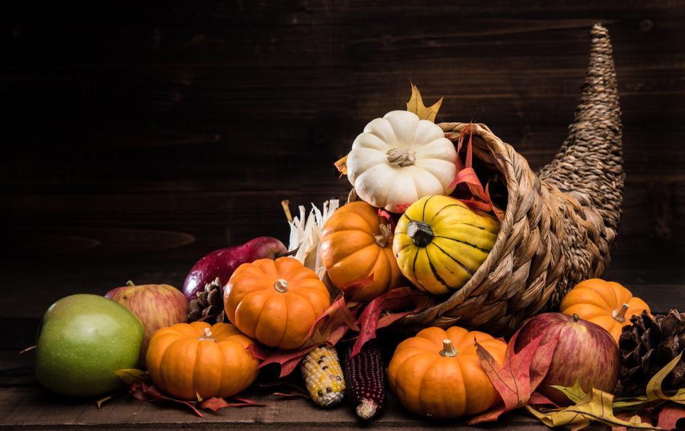 An overflowing horn of plenty. A horn of plenty filled with the symbols of Thanksgiving including corn and pumpkins against a black background.