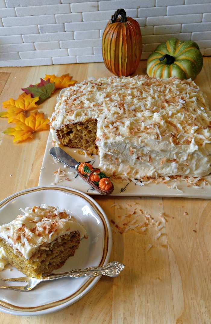 Pumpkin cake for Thanksgiving. A pumpkin dessert recipes for Thanksgiving consisting of a pumpkin cake with toasted coconut frosting - a slice is cut from the cake an on a plate in the foreground, and the whole cake is in the background next to fake pumpkins and fake leaves.
