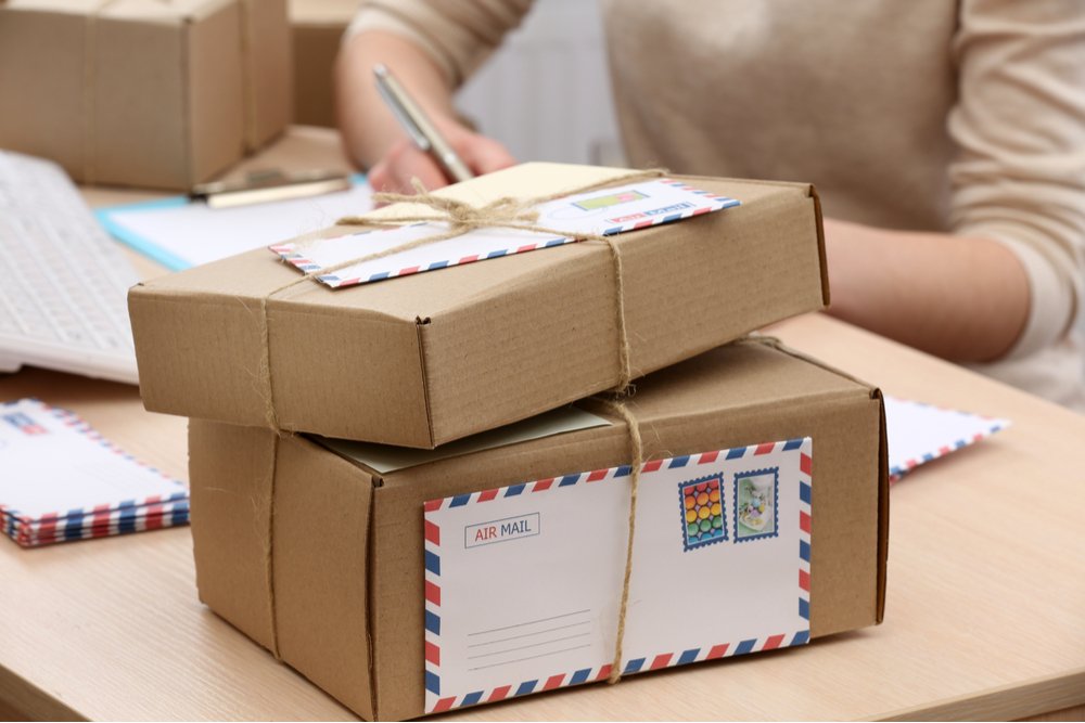 Packages and letters. Two paper wrapped packages and air mail envelopes waiting for the woman sitting behind them at the table to write on Santa Clause address on the packages.