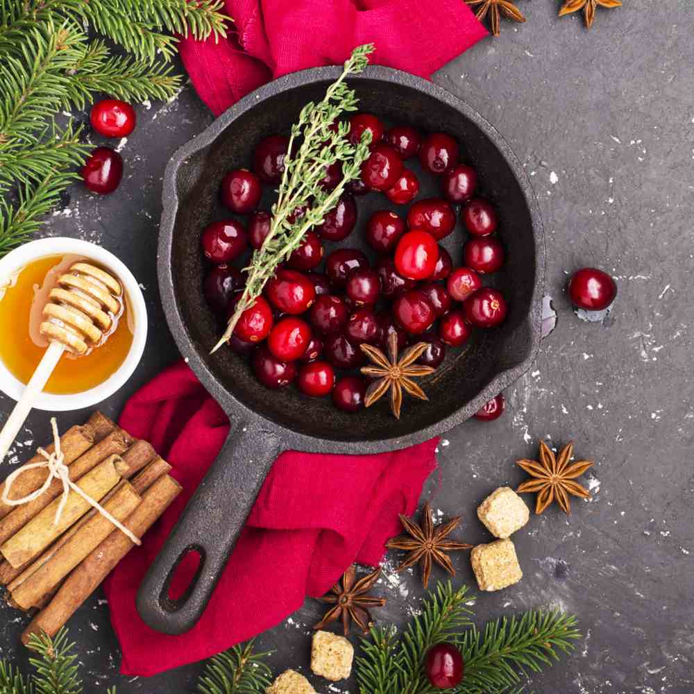 Cranberries in a cast iron pan. A cast iron pan of cranberries next to various spices and herbs to start a cranberry recipe for Thanksgiving.