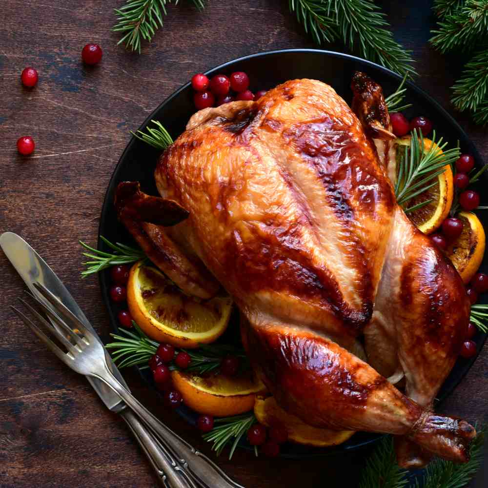 Thanksgiving turkey on a table. A Thanksgiving turkey with oranges, cranberries and rosemary on a Thanksgiving table next to a set of cutlery.