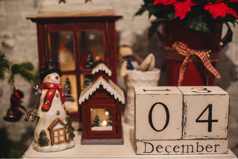 December 4 blocks and Christmas decor. Wooden blocks that read "December 4" on a table next to various Christmas trinket decorations and a poinsettia plant in a jug.