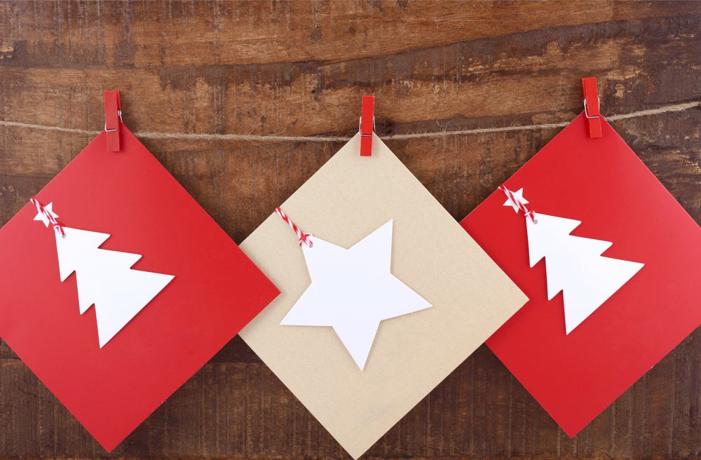 Three Christmas cards on a string Three Christmas cards (two red with white trees and one beige with a white star) hanging on a line with red clothespins.