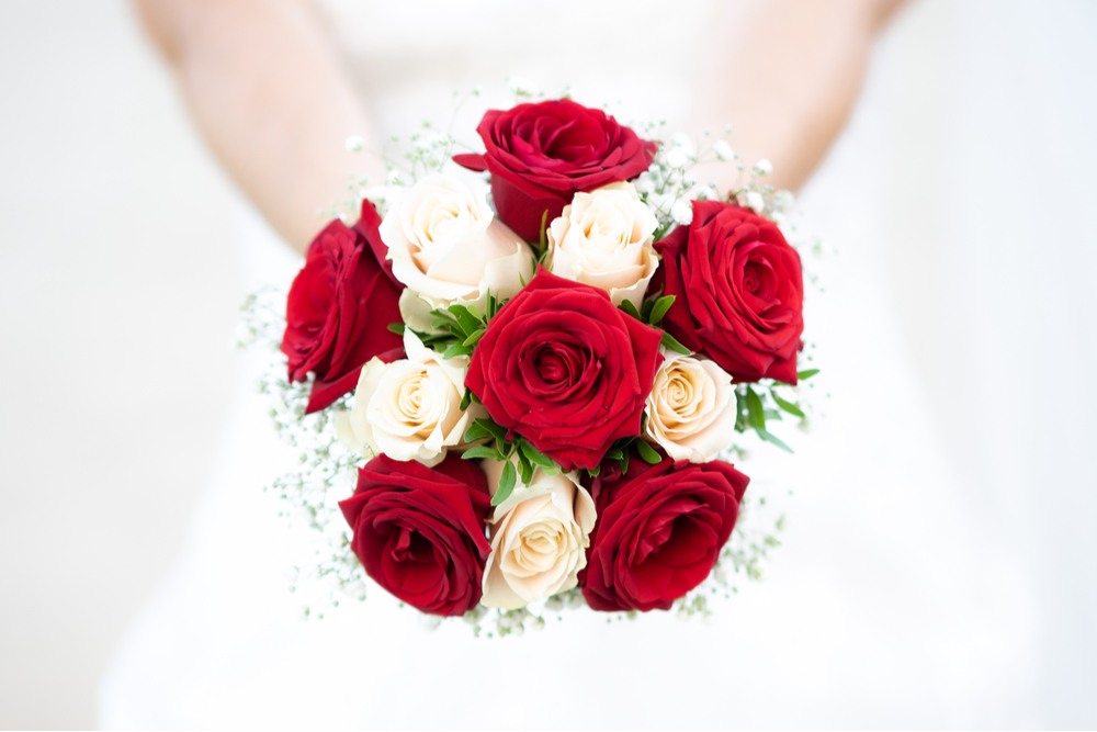 Red and white bridal bouquet A woman in a wedding dress holding a bouquet of red and white roses, meaning unity and eternal love.