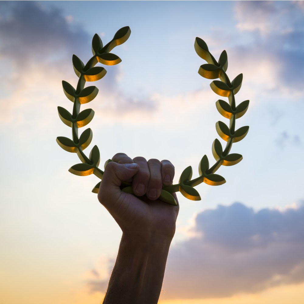 Hand holding laurel wreath A hand holding a laurel wreath, one of the symbols of Apollo against a sky background that where the sun is setting and the sky is changing colors from blue to orange.